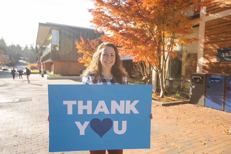 Woman holding a blue sign depicting the phrase Thank You